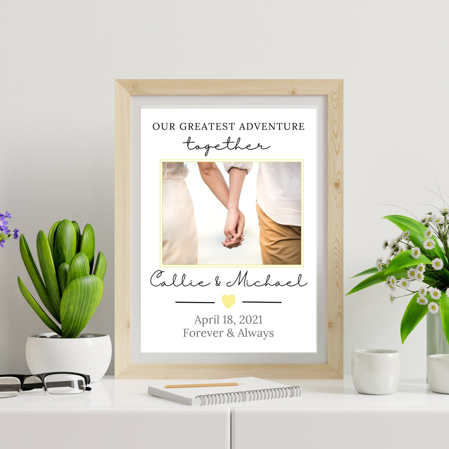 Framed print with a couple's photo and personalized text on a white surface with plants.