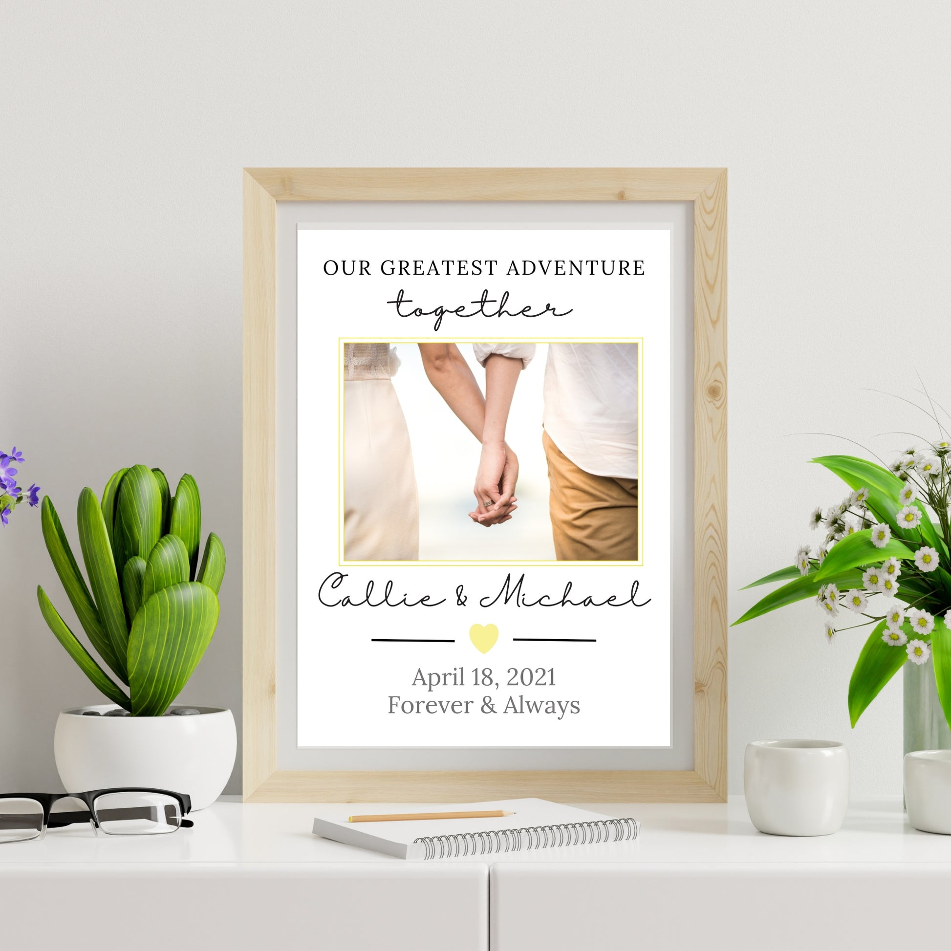 Framed print with a couple's photo and personalized text on a white surface with plants.